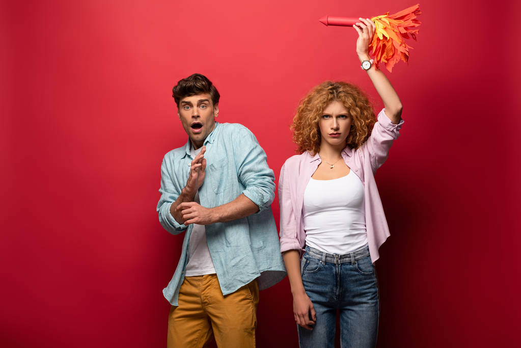 curly confident woman holding little rocket near scared man, on red - Photo, Image