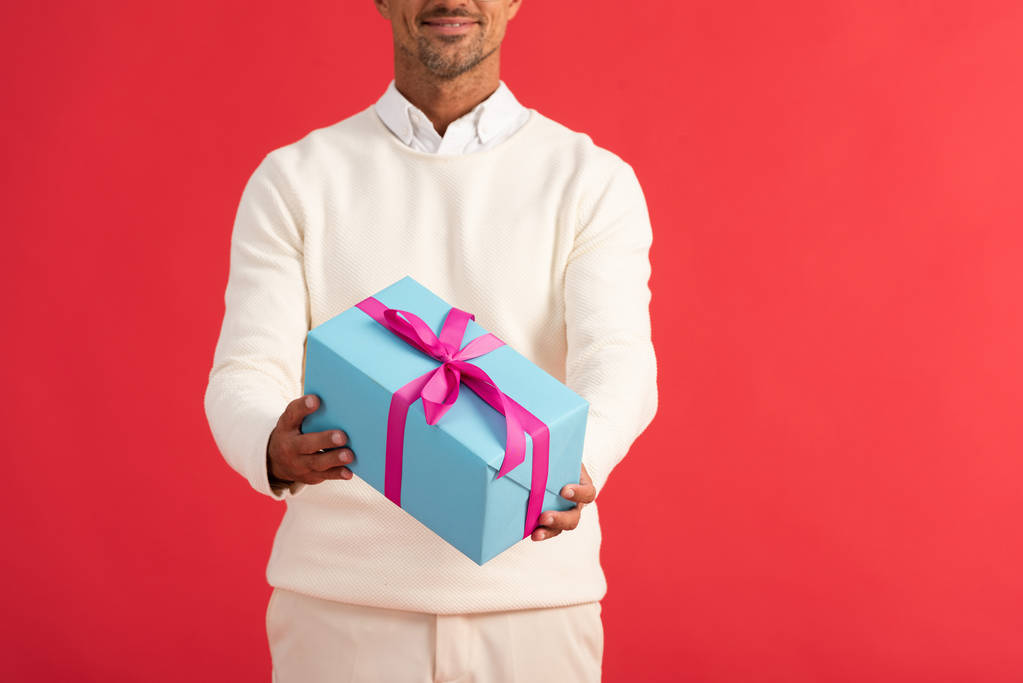 обрізаний вид усміхненого чоловіка, що тримає подарункову коробку ізольовано на червоному
  - Фото, зображення