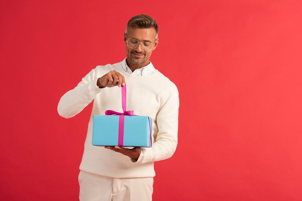 щасливий чоловік тримає подарункову коробку ізольовано на червоному
  - Фото, зображення
