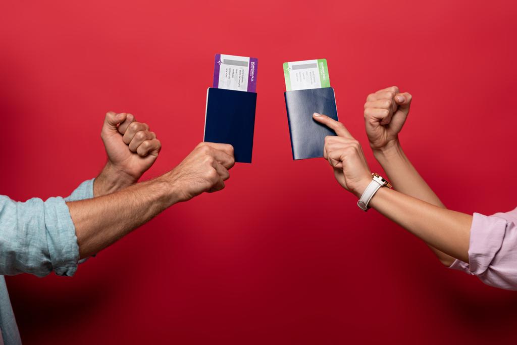 partial view of travelers holding fists and passports with air tickets, isolated on red - Photo, Image