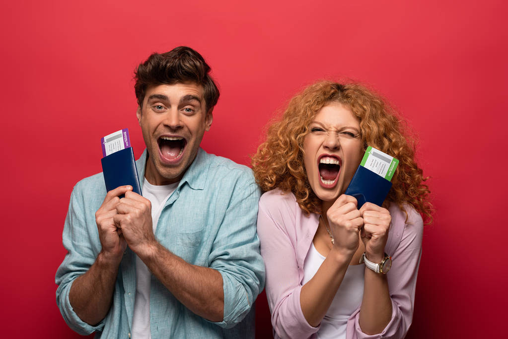 couple de voyageurs excités criant et tenant des passeports avec des billets d'avion, isolé sur rouge
 - Photo, image
