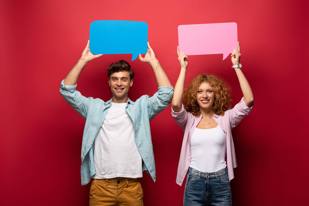 smiling couple holding pink and blue speech bubbles, on red - Photo, Image