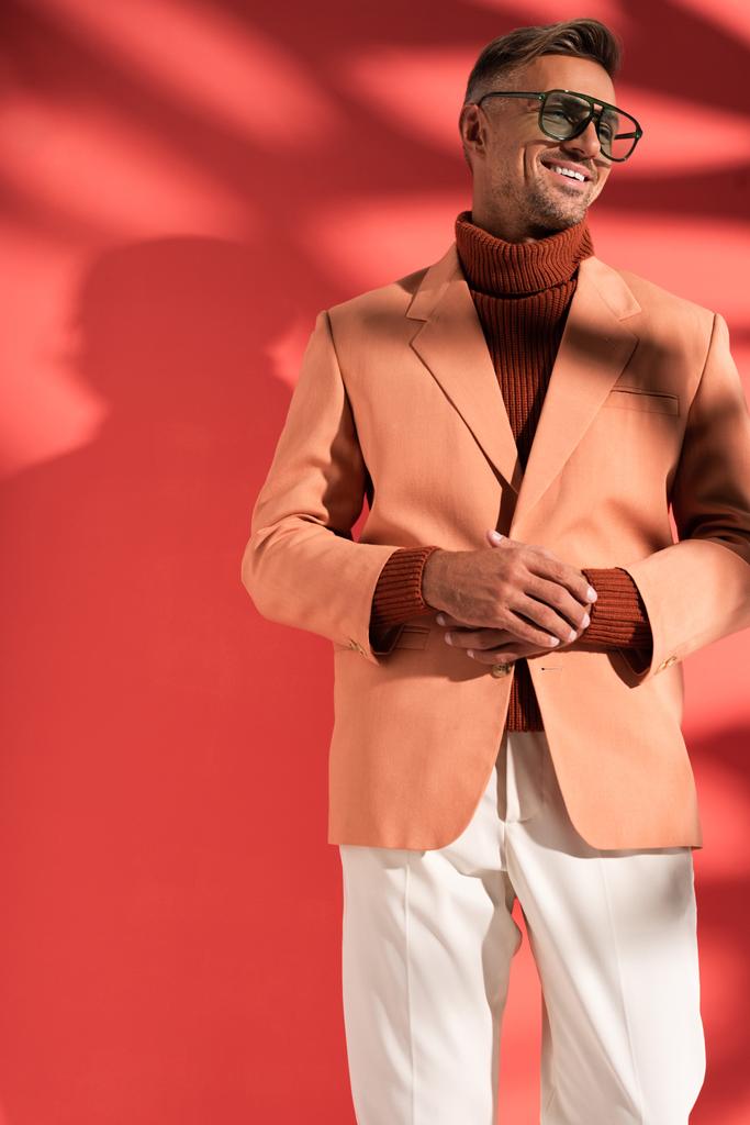 hombre de moda en gafas de sol y chaqueta de pie en rojo con sombras
  - Foto, Imagen