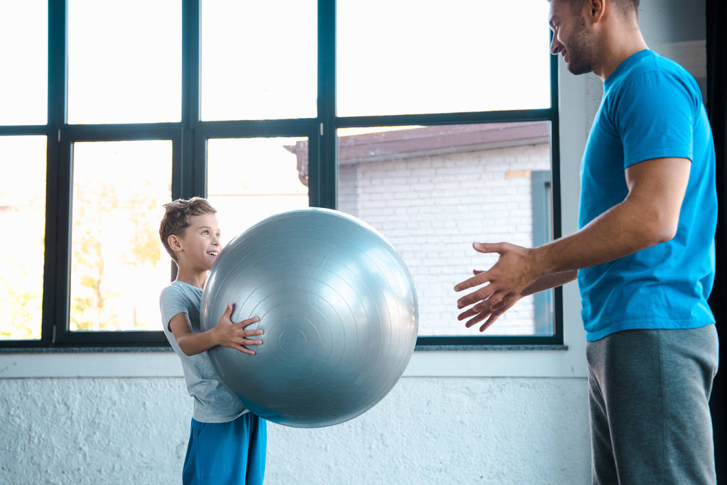 Spor salonunda elinde spor topu tutan tatlı bir çocuk ve babasına bakıyor.  - Fotoğraf, Görsel