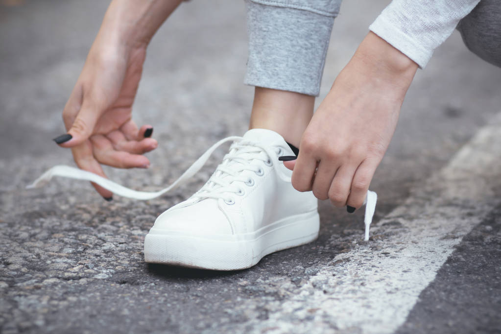 tyttö kyykyssä alas sitoa kengännauhat valkoinen lenkkarit asfalttitiellä, syksyn urheilu käsite ulkona
 - Valokuva, kuva