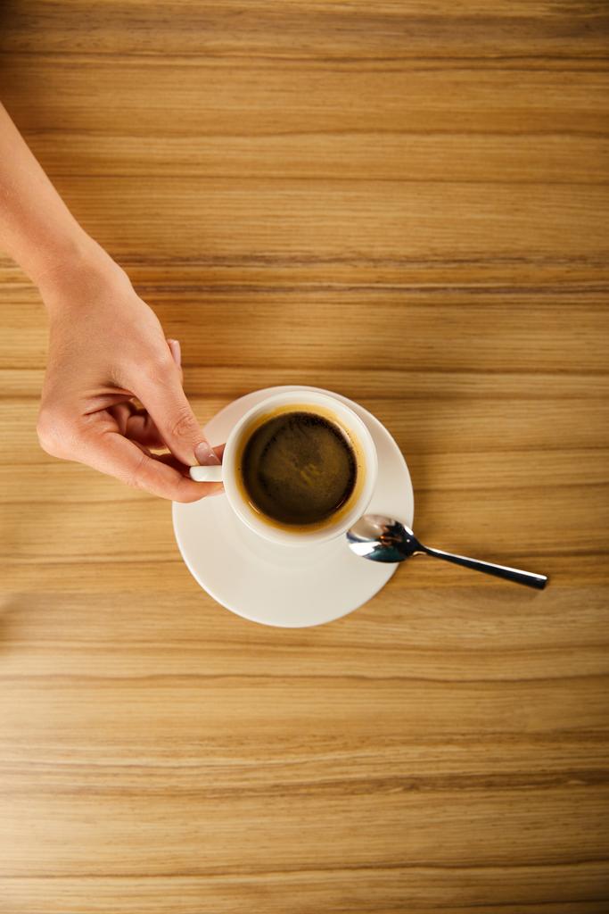 vrchní pohled na ženu držící šálek kávy v kavárně  - Fotografie, Obrázek