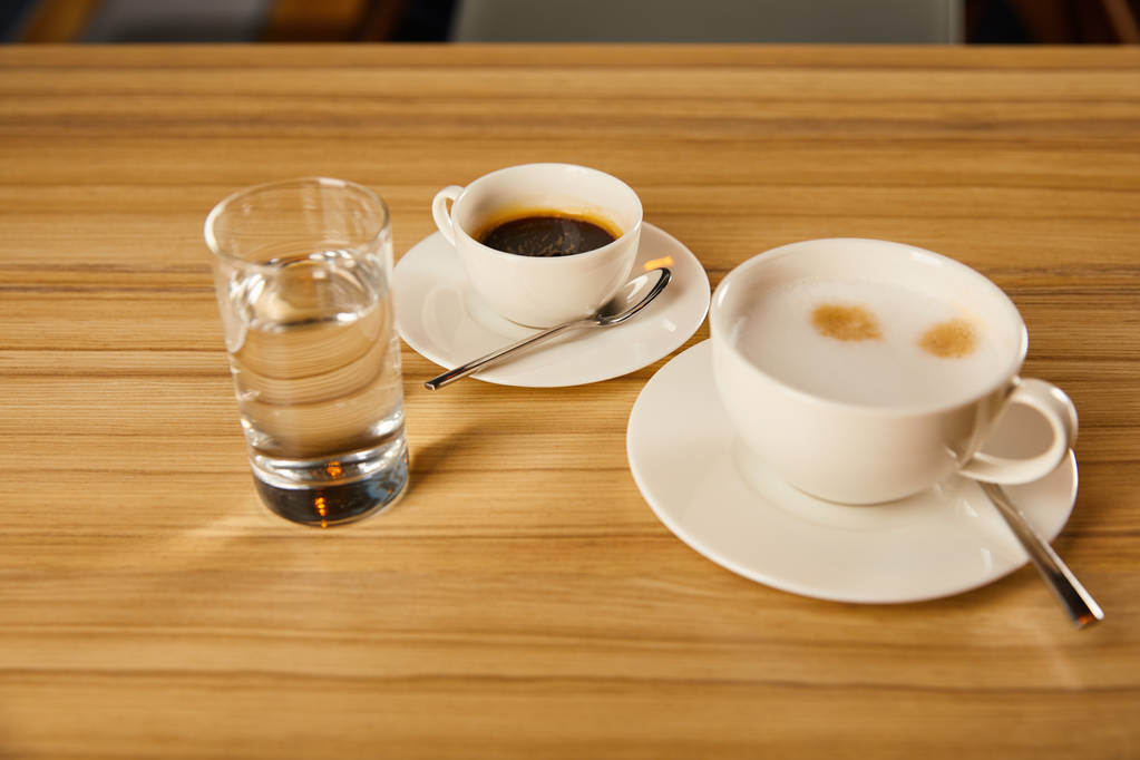 kopjes met koffie bij glas water in café  - Foto, afbeelding