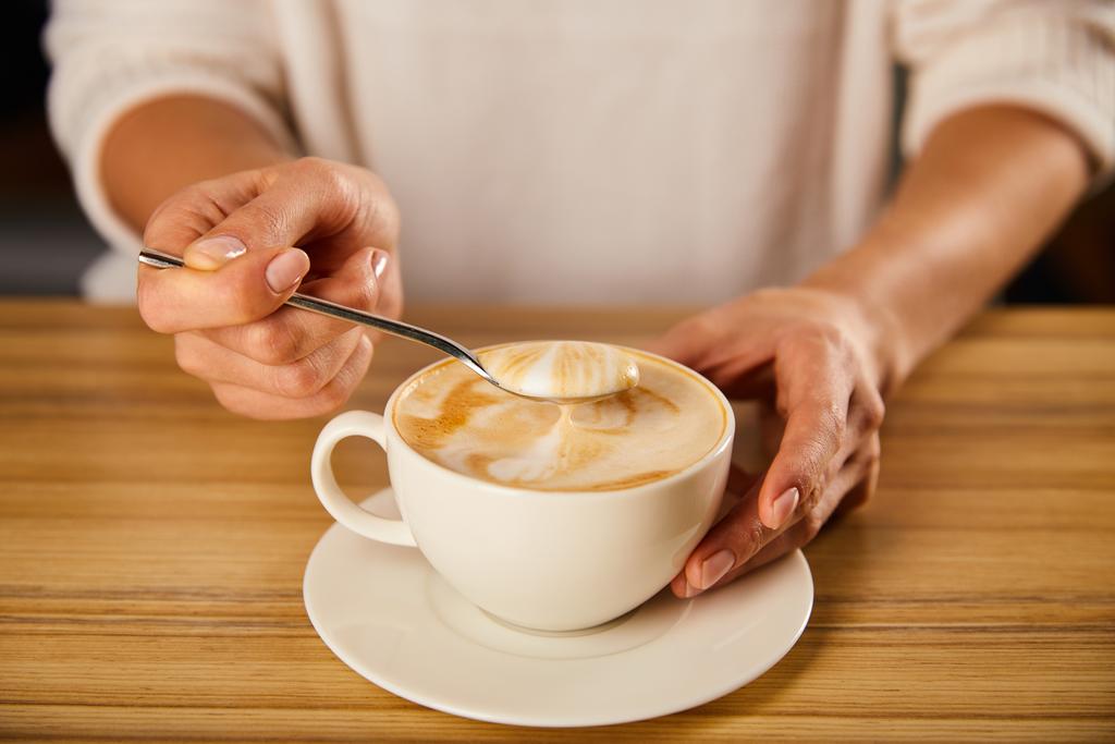 cropped view of woman holding spoon with cappuccino foam - Photo, Image