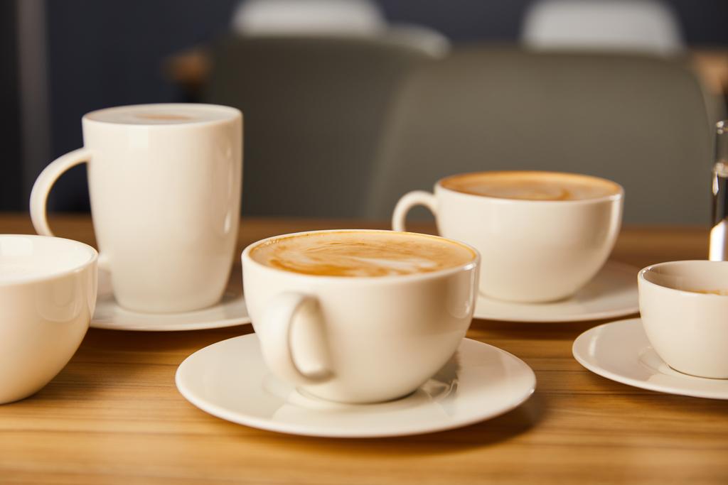 selektiver Fokus der Untertassen mit weißen Tassen leckeren Kaffee im Café  - Foto, Bild