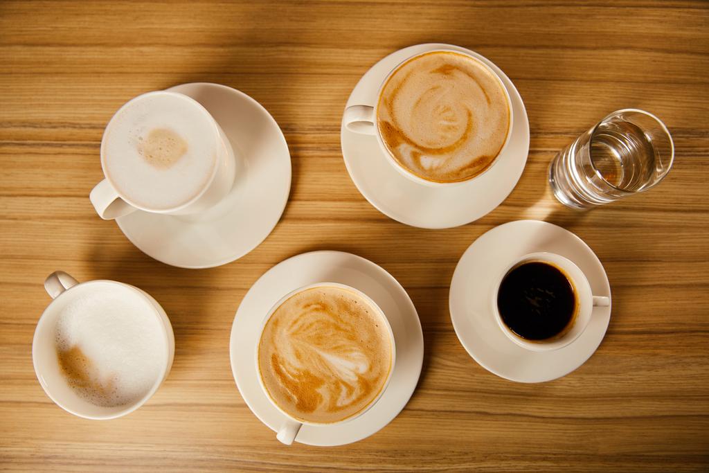 vista superior de platillos con tazas de café diferentes cerca de un vaso de agua
  - Foto, imagen
