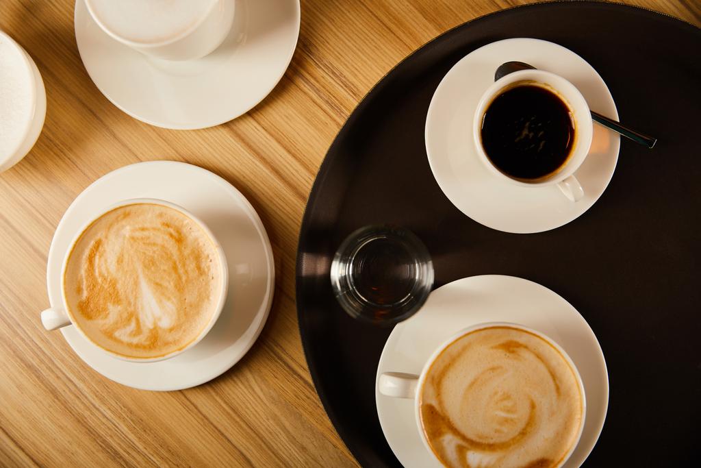 top view of cups of different coffee near glass of water on tray  - Photo, Image