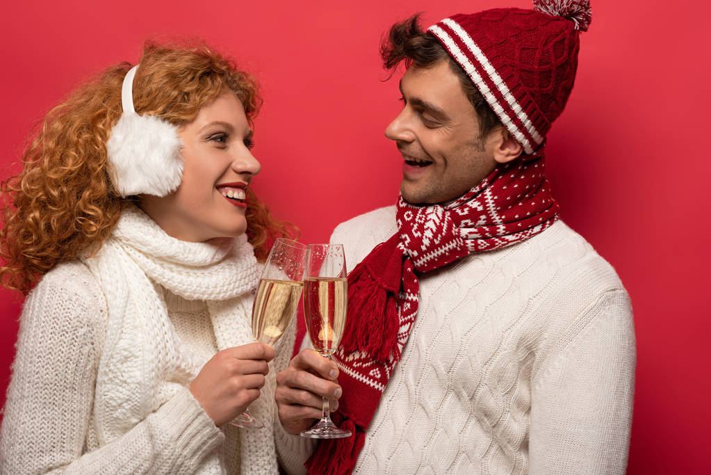 beautiful smiling couple in winter outfit clinking with champagne glasses, isolated on red - Photo, Image
