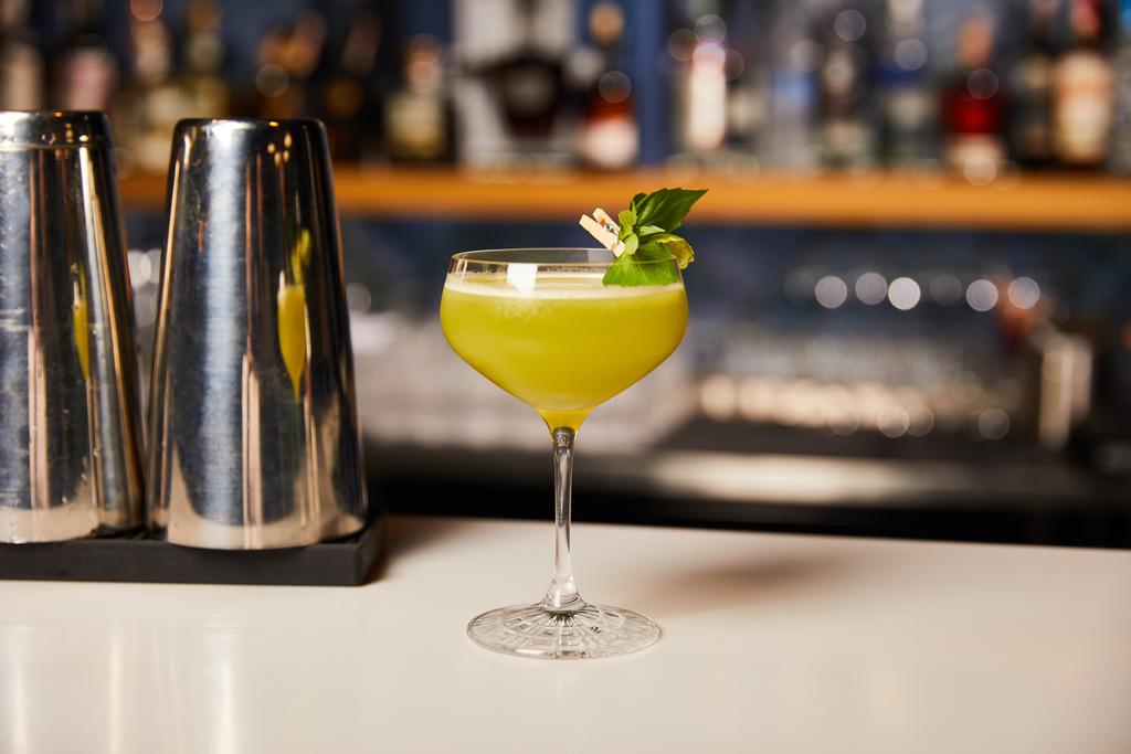 glas met verse alcoholcocktail in de buurt van shaker op bar  - Foto, afbeelding