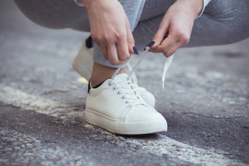 meisje gekraakt naar strik schoenveters op witte sneakers op asfalt weg, herfst sport concept buiten - Foto, afbeelding