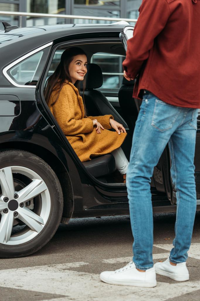 Водій таксі відкриває двері автомобіля усміхненій молодій жінці
 - Фото, зображення