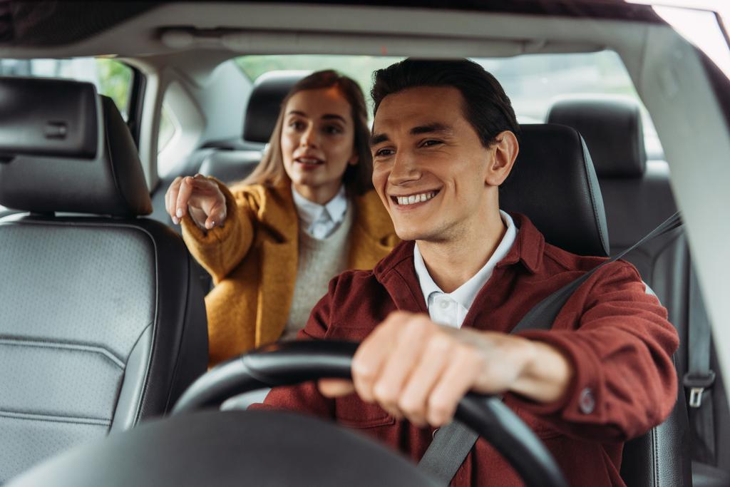 Motorista de táxi sorridente com mulher passageira apontando na estrada
  - Foto, Imagem