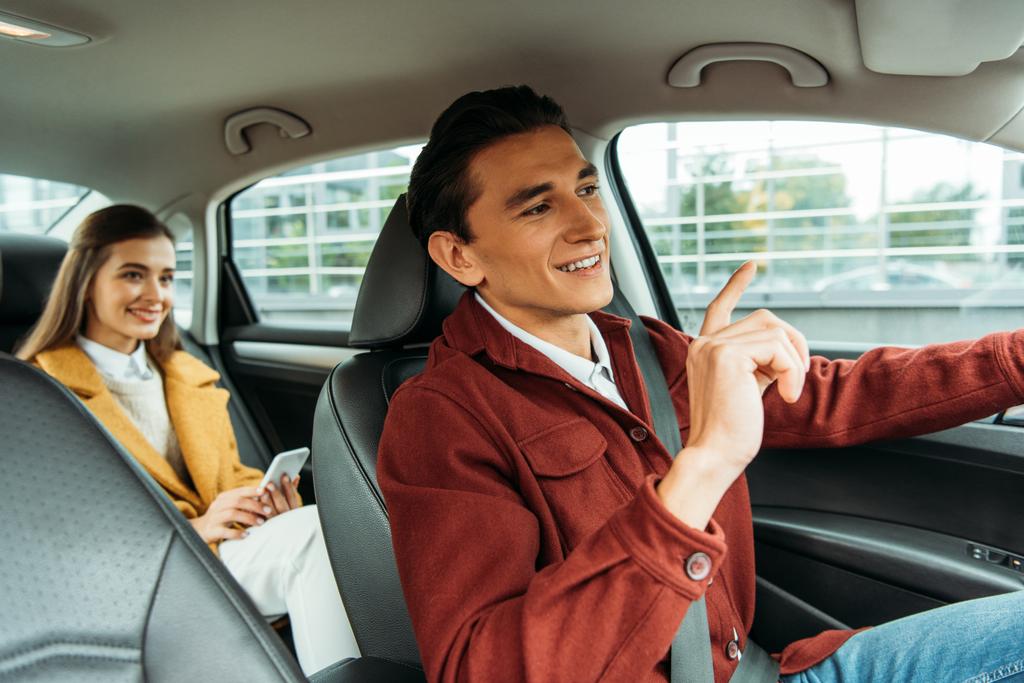 笑顔のタクシー運転手と車の中でスマートフォンを持つ乗客 - 写真・画像