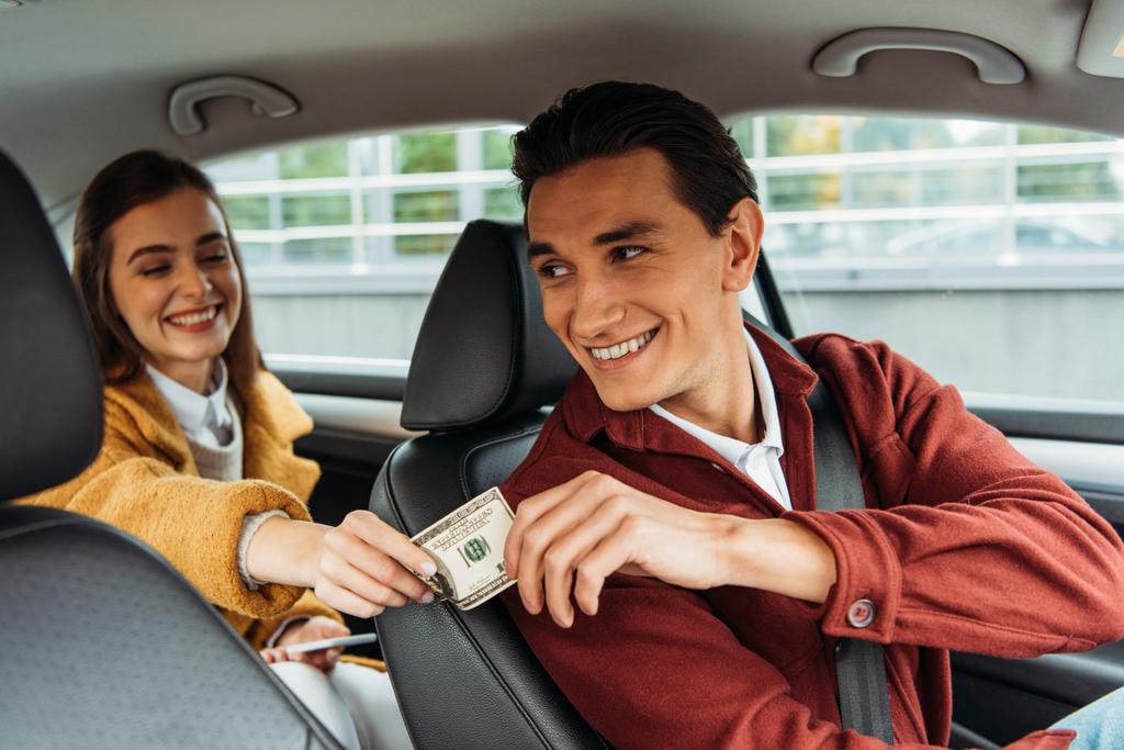 Jonge vrouw passagier geeft geld aan glimlachende taxichauffeur - Foto, afbeelding