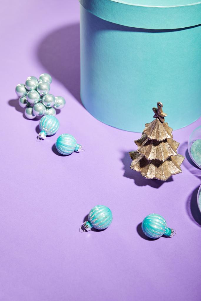 голубая подарочная коробка и декоративная елка с безделушками на фиолетовом фоне
 - Фото, изображение