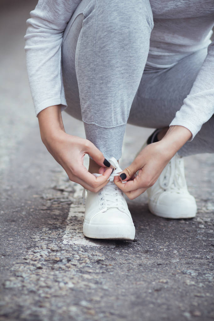 fille accroupi vers le bas pour attacher lacets sur chaussures blanches sur route asphaltée, concept de sport d'automne en plein air
 - Photo, image