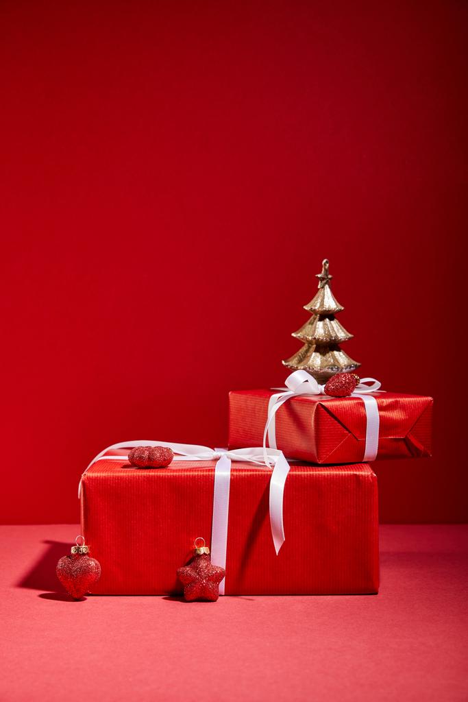 красные подарочные коробки и декоративная золотая елка с безделушками на красном фоне
 - Фото, изображение