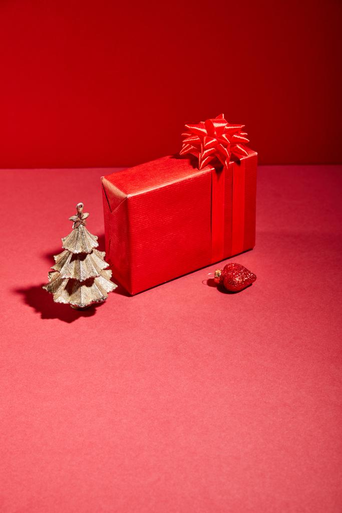 красный подарочная коробка и декоративная золотая елка с безделушкой на красном фоне
 - Фото, изображение