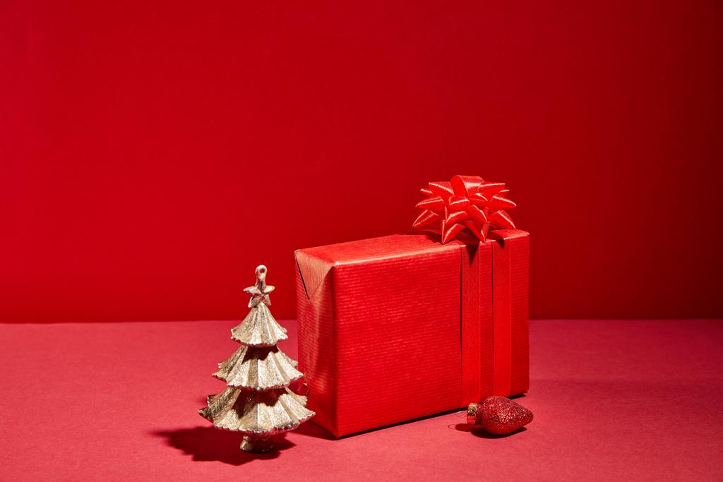 piros ajándék doboz és dekoratív arany karácsonyfa csecsebecsével piros háttér - Fotó, kép