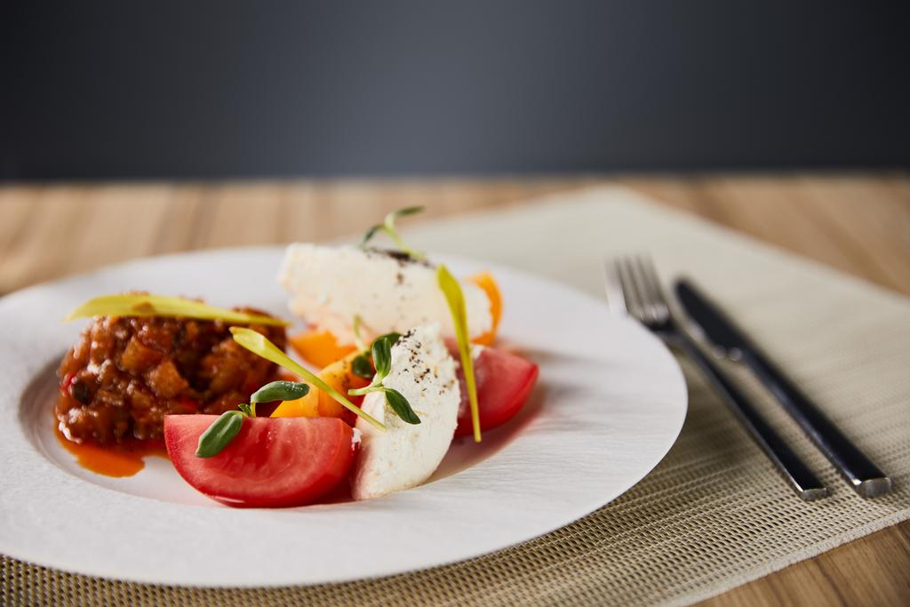 enfoque selectivo de delicioso plato de restaurante con caviar de berenjena y tomates servidos en mesa de madera con cubiertos aislados en gris
 - Foto, Imagen