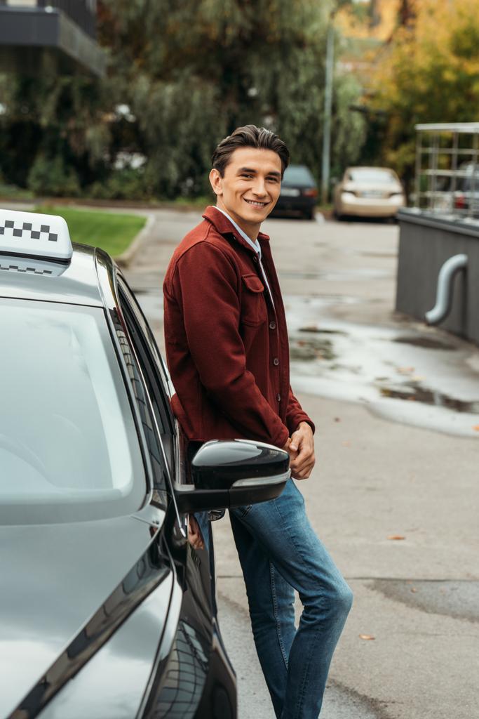Lächelnder Taxifahrer blickt in Kamera neben Auto - Foto, Bild