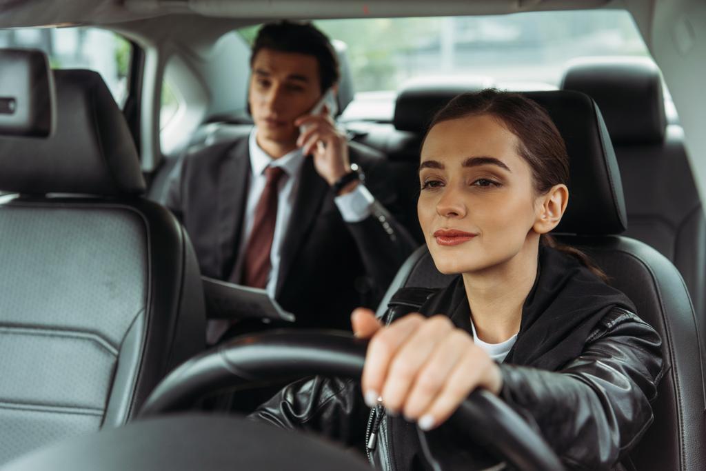 Mujer taxista sosteniendo el volante mientras el hombre de negocios habla en el teléfono inteligente
 - Foto, Imagen