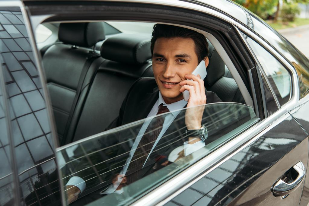 笑顔のビジネスマンがタクシーの後部座席でスマートフォンで話している ロイヤリティフリー写真 画像素材