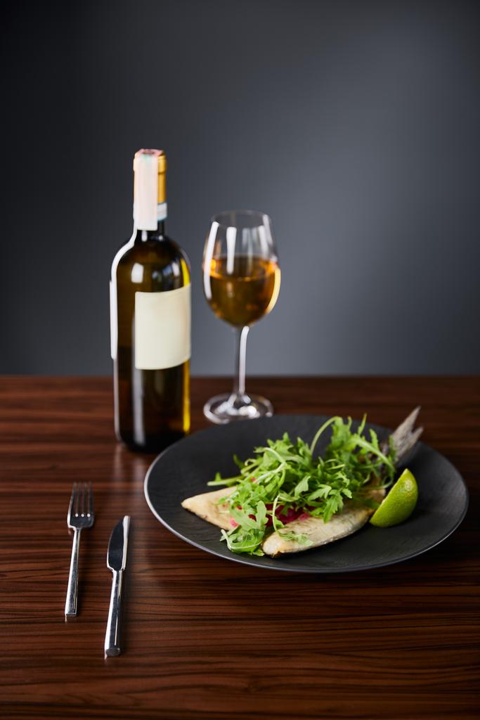 Limonlu balık bifteği ve ahşap masada çatal bıçak takımı ve siyah arka planda beyaz şarap. - Fotoğraf, Görsel