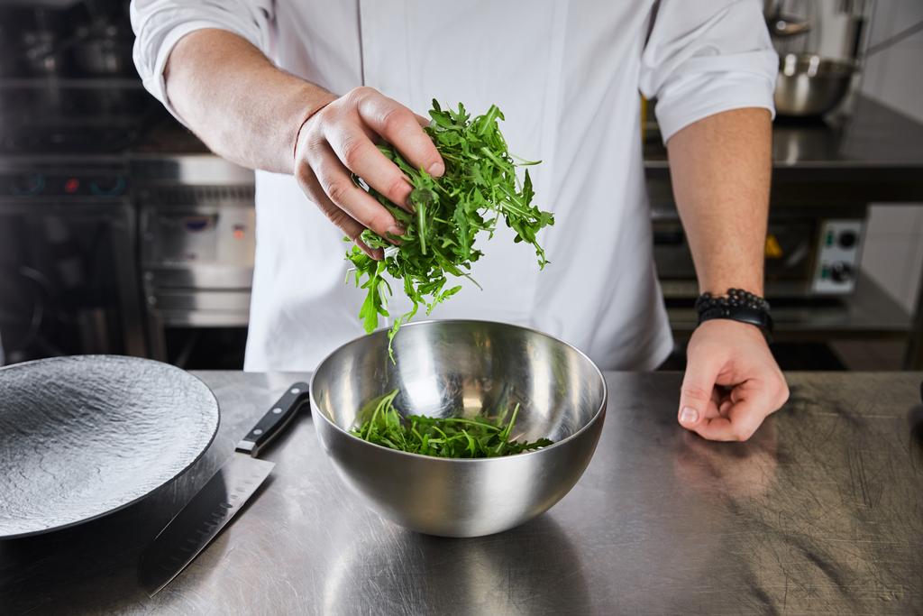 cropped view of chef cooking salad with arugula at kitchen in restaurant - Photo, Image