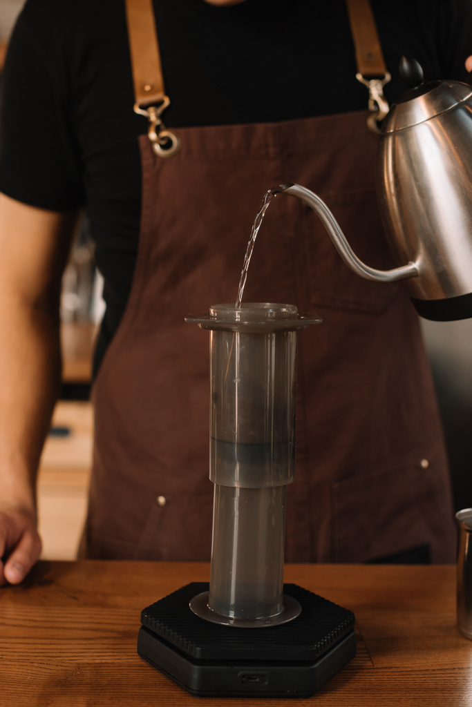 обрезанный вид на бариста, наливающий воду из чайника в аэропрессе во время приготовления кофе
 - Фото, изображение