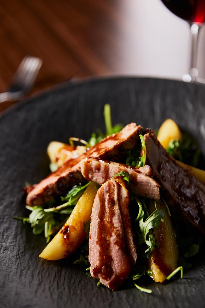 közeli kilátás ízletes meleg saláta arugula, burgonya és hús fekete lemez fa asztalon - Fotó, kép