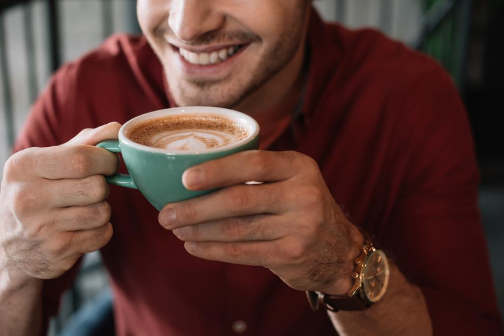 rajattu näkymä hymyilevä nuori mies kuppi maukasta cappuccino kahvilassa
 - Valokuva, kuva