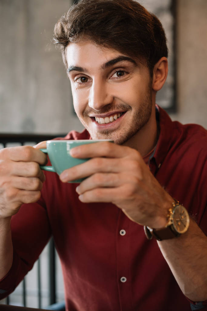 jovem sorridente com xícara de cappuccino saboroso no café
 - Foto, Imagem