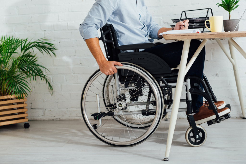 Oříznutý pohled na muže v invalidním vozíku psaní v notebooku na pracovišti - Fotografie, Obrázek
