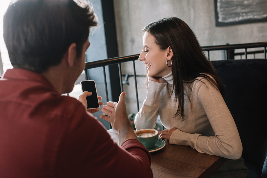 χαρούμενος άνθρωπος δείχνει κορίτσι οθόνη smartphone, ενώ πίνοντας καφέ στο μπαλκόνι στην καφετέρια - Φωτογραφία, εικόνα