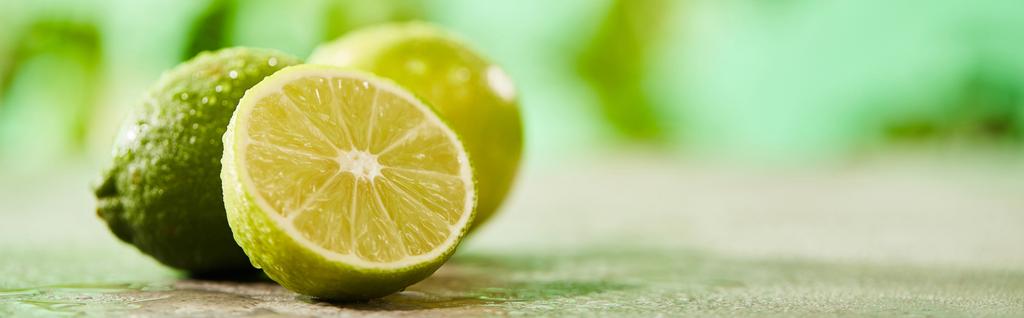 panoramic shot of whole and cut limes with drops on marble surface  - 写真・画像