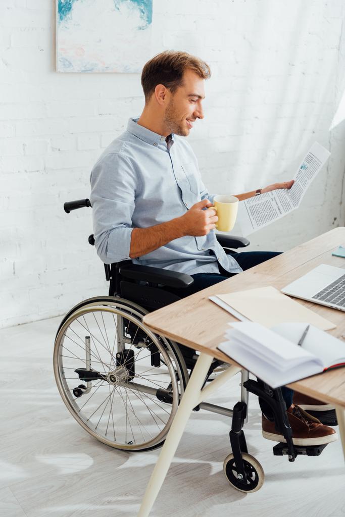Bonheur homme en fauteuil roulant boire du thé et lire le journal au bureau
 - Photo, image