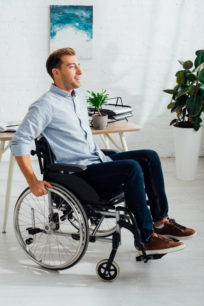 Χαμογελώντας άνθρωπος σε αναπηρική καρέκλα και κοιτάζοντας μακριά στο σαλόνι - Φωτογραφία, εικόνα