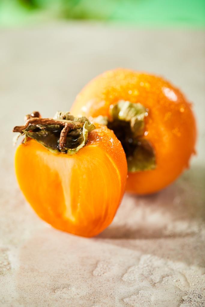 selective focus of whole and cut persimmons on marble surface  - 写真・画像