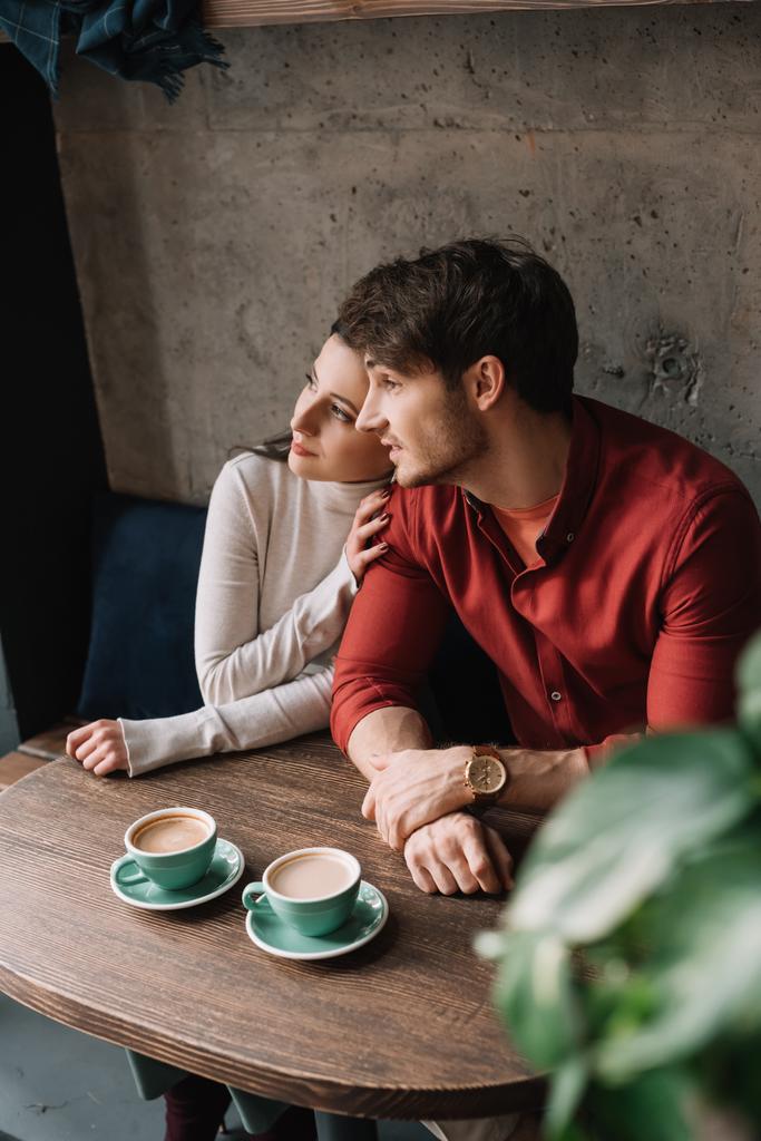 szelektív fókusz zöld levelek és romantikus fiatal pár ölelés és kávézás a kávézóban - Fotó, kép