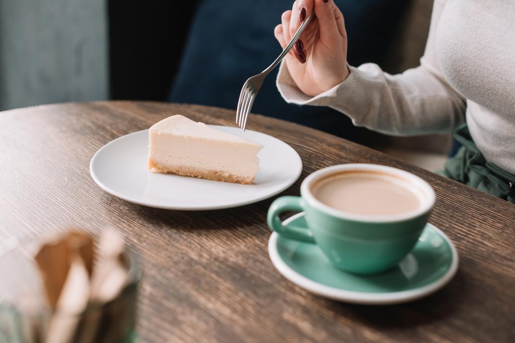 vista parcial de la mujer comiendo pastel de queso con tenedor y beber café en la cafetería
 - Foto, imagen