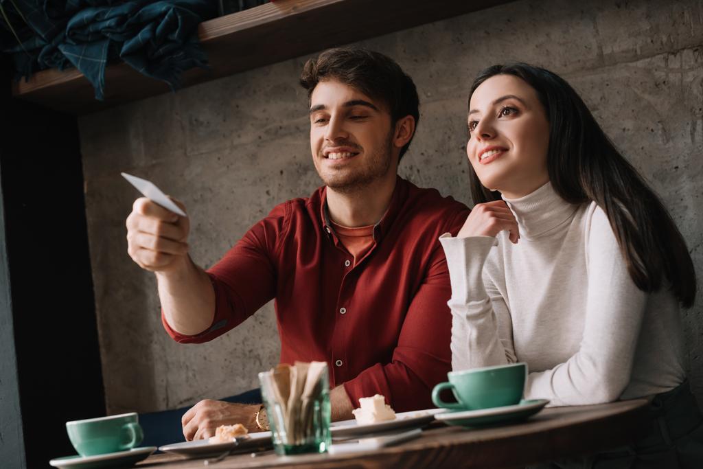 若い夫婦はコーヒーショップでクレジットカードを持ちながらチーズケーキとコーヒーを飲む - 写真・画像