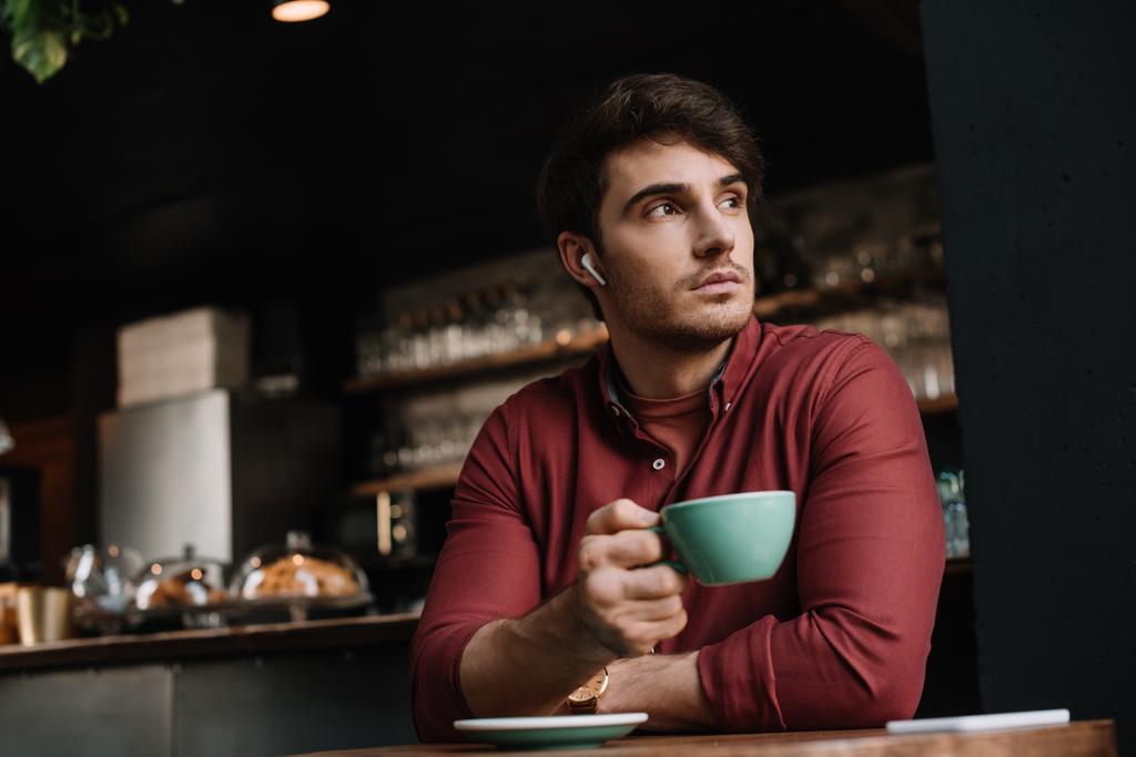 zamyšlený muž v bezdrátových sluchátkách pije kávu v kavárně - Fotografie, Obrázek