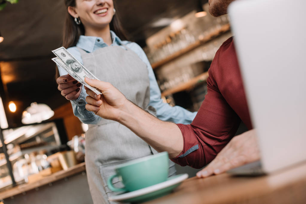 Bilgisayarlı serbest çalışanın kahve dükkanındaki gülümseyen garsona para vermesi. - Fotoğraf, Görsel
