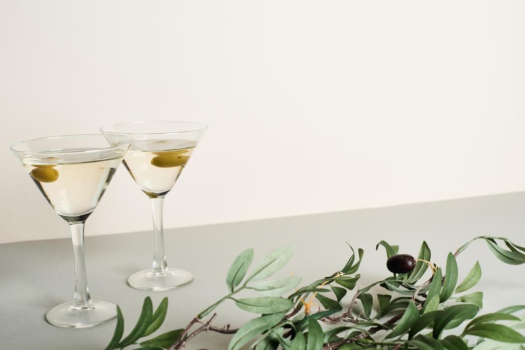 Two glasses with cocktails and olive branch on grey surface isolated on white - Photo, Image