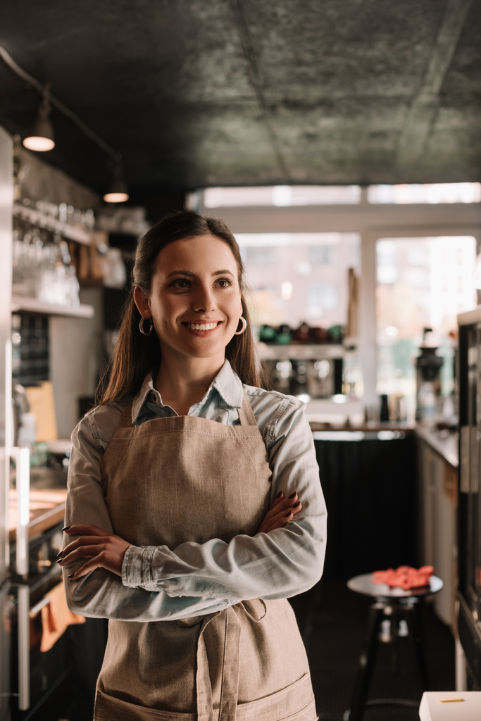 smiling barista in apron standing in cafe with crossed arms - Photo, Image